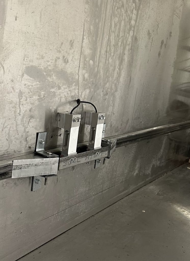 photo of closeup of installed load cells in food waste measurement system. it shows ramps that guide load bearing wheels onto a thin metal bar attaching two load cells at their load point. This bar completes the wheel track where the load cells are positioned.