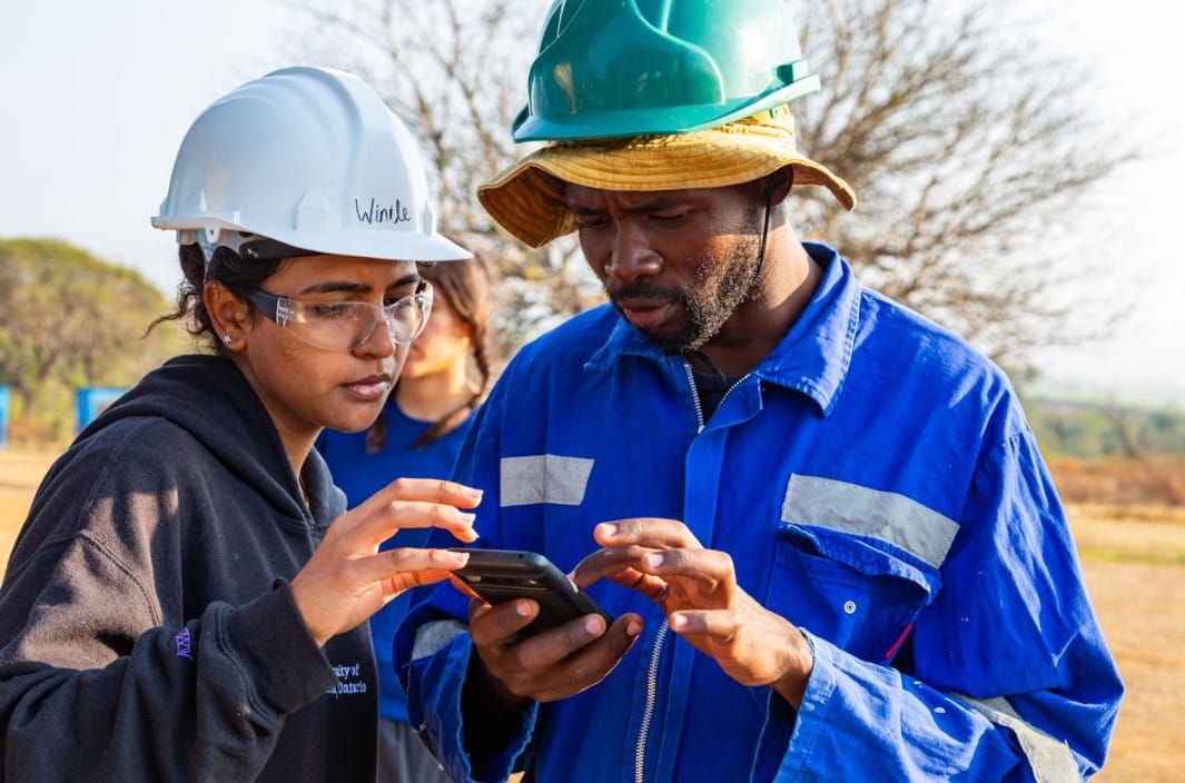two people from the elbows up looking at a controller app on a smartphone. Both are wearing hardhats