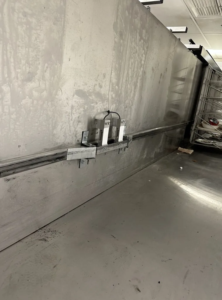 Photo of ramps along wheel track behind rotating cafeteria tray return racks that guide the rear wheels of the rotating tray system onto the load points of load cells measuring the weight of the assembly with returned trays