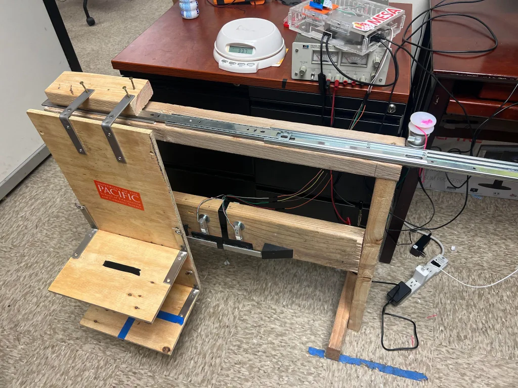 Photo of food waste measuring system test mock-up. The mock-up is made of plywood and 2 by 4s and shows testing of the load cell mounting system and ramps that guide the wheels along the wheel track to the load cell load points